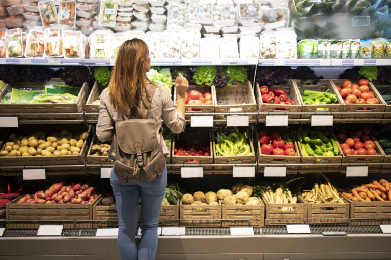 Good Looking Woman Standing In Front Of Vegetable Shelves Choosing What To Buy.