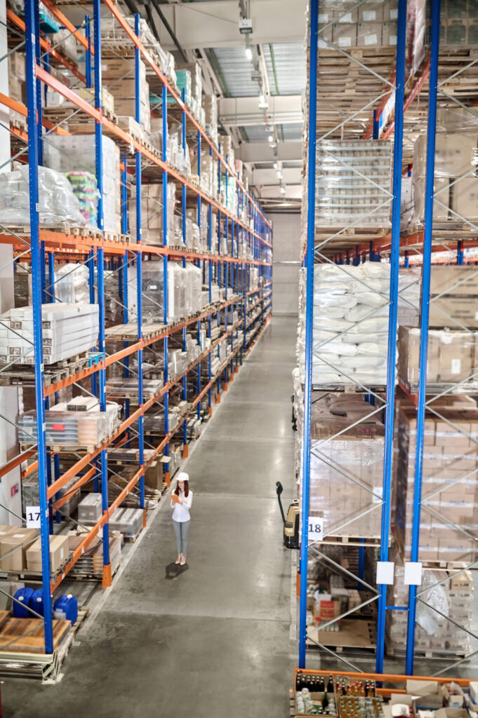 Woman With Tablet Standing In Large Industrial Warehouse